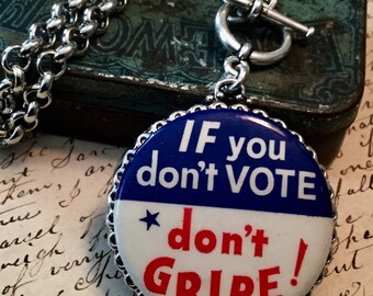 May include: A silver chain necklace with a toggle clasp and a blue, white, and red button pendant. The button has the text "IF you don't VOTE *don't GRIPE!"