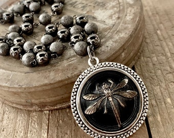 May include: A silver necklace with a black and silver dragonfly pendant. The necklace is made of small, round beads.