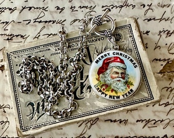 May include: A silver chain necklace with a round pendant featuring a vintage illustration of Santa Claus. The pendant has the text "Merry Christmas Happy New Year".