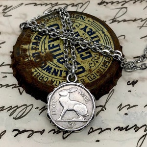 May include: A silver chain necklace with a silver pendant featuring a 1962 Irish 3 pence coin with a hare design. The coin has the inscription "REUL" and "3d".