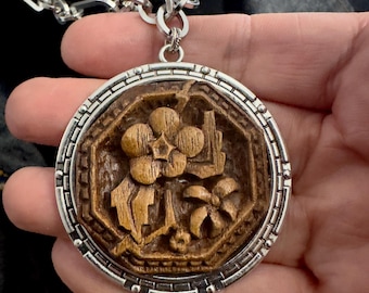 May include: A circular pendant featuring a carved brown wooden center with a floral motif set inside a silver-toned metal frame with a geometric border. The pendant hangs from a thick, chunky silver-toned metal chain link necklace.