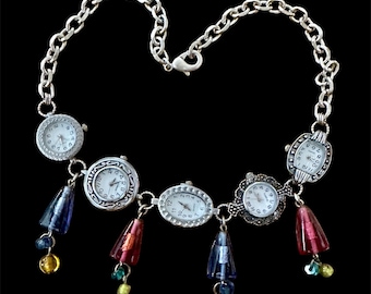 May include: A silver necklace with multiple small watch faces and colorful dangling beads. The necklace has a silver chain and a clasp.