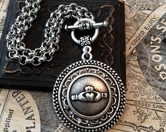 May include: Silver Celtic knot pendant necklace with a toggle clasp. The pendant features a detailed design of an intertwined knot with a heart in the center. The necklace is on a silver chain.