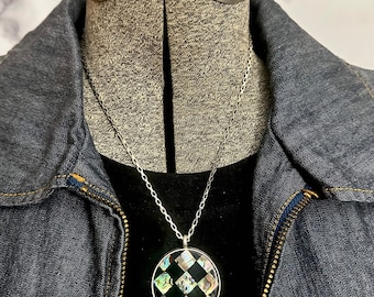 May include: A silver chain necklace with a round pendant featuring a black and white checkered pattern with iridescent accents.