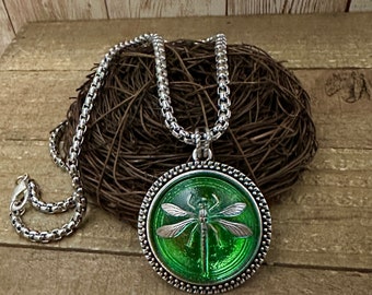 May include: A silver chain necklace with a green glass pendant featuring a silver dragonfly. The pendant is surrounded by a silver beaded border.