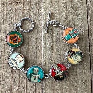 May include: A silver bracelet with six round charms featuring vintage robot illustrations. The charms are attached to a silver chain with a toggle clasp.
