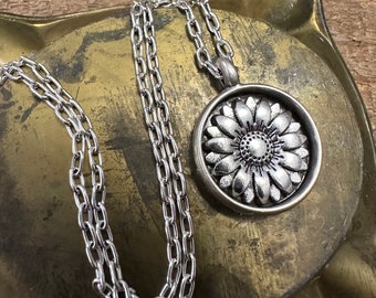 May include: A silver chain necklace with a round pendant featuring a detailed sunflower design.