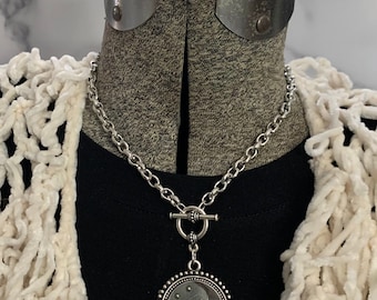 May include: A silver chain necklace with a silver toggle clasp and a round pendant featuring a crescent moon and stars.