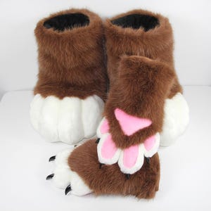 May include: A pair of brown and white faux fur animal paw boots and a matching pair of fingerless paw gloves. The boots feature white toes and brown fur, while the gloves have brown fur, white paw pads, pink accents, and black claws.