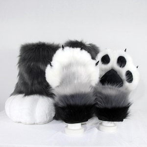 May include: A pair of plush animal paw gloves featuring long, shaggy faux fur in shades of dark grey, light grey, and white. The palms are white with black paw pads and pointed black claws extending from the tips of the fingers.