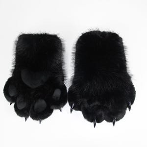 Puede incluir: Un par de guantes de piel sintética negra diseñados como patas de animal. Los guantes presentan pelo sintético negro largo y suave, almohadillas negras lisas en la palma y garras de plástico negro puntiagudas en cada punta de los dedos.