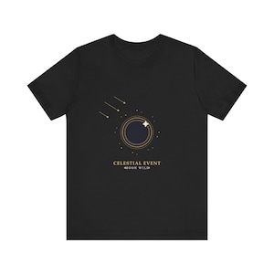 Op de afbeelding: Een zwart t-shirt met korte mouwen en een afbeelding van een donkere cirkelvormige maan omringd door dunne gouden ringen en een vierpuntige ster. Boven de maan staan drie gouden vallende sterren. De tekst luidt CELESTIAL EVENT en MOON WILD.