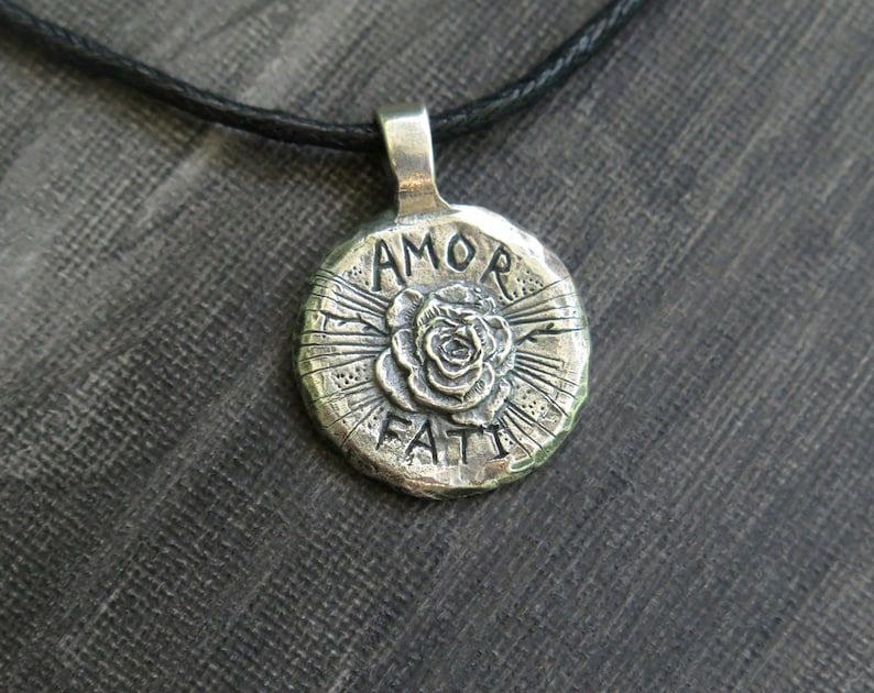 May include: Silver pendant necklace with a round charm featuring a rose and the words "AMOR FATI" in a stylized font.