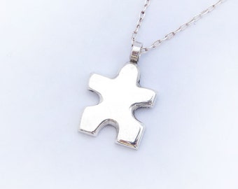 Puede incluir: Un collar de cadena de plata con un colgante de pieza de rompecabezas de plata.