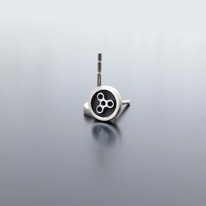May include: A pair of silver stud earrings with a black circular design featuring a stylised three-pointed star.