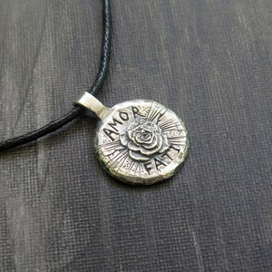 May include: Silver necklace with a round pendant featuring a rose and the words "Amor Faith".