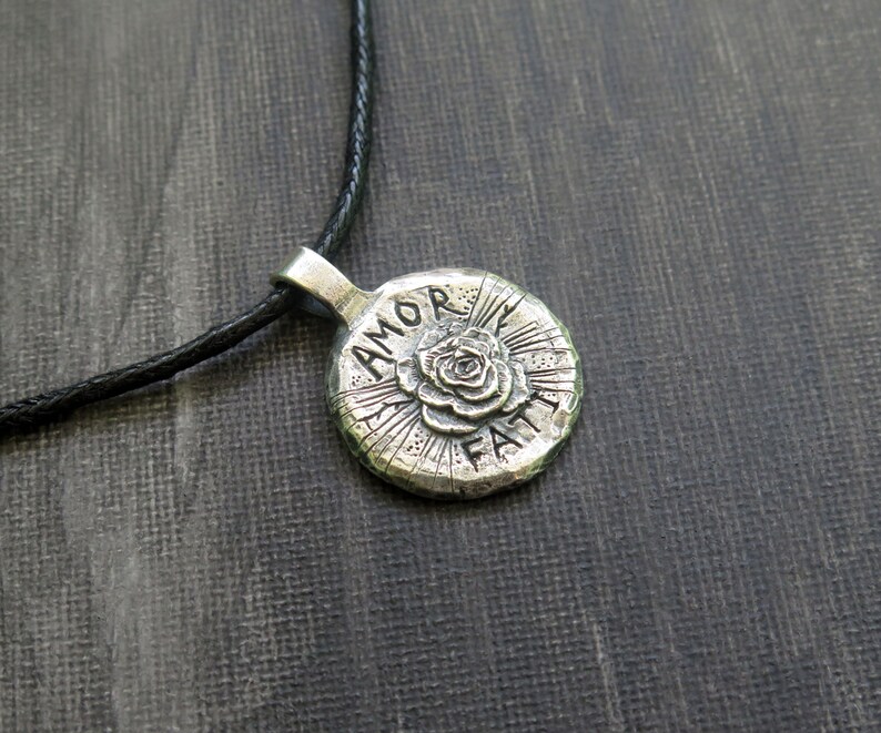 May include: Silver necklace with a round pendant featuring a rose and the words "Amor Faith".