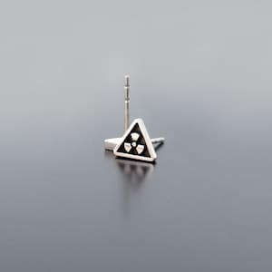 May include: A silver triangle earring with a black radiation symbol in the center.
