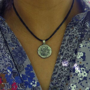 May include: A silver necklace with a round pendant featuring a rose and the words "AMOR FATI" on a black cord.