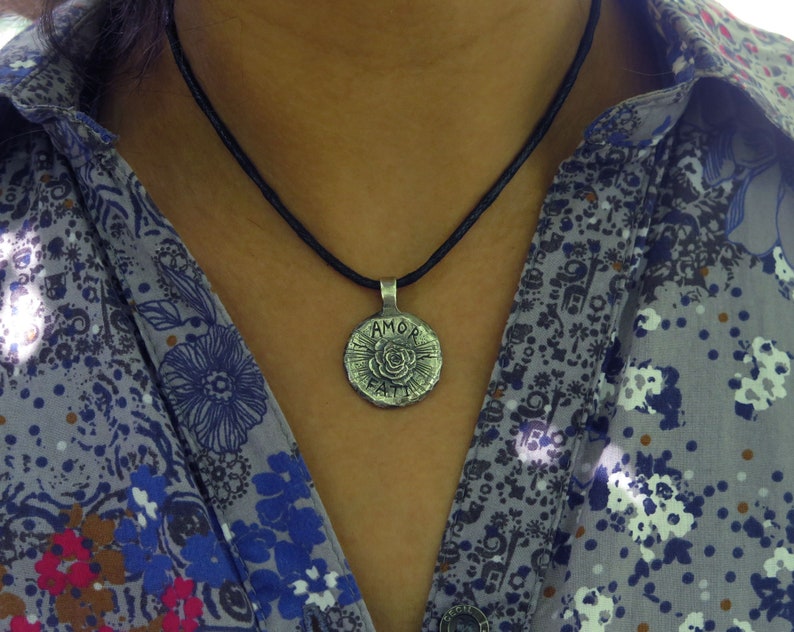 May include: A silver necklace with a round pendant featuring a rose and the words "AMOR FATI" on a black cord.
