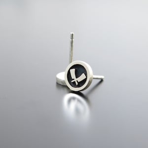 May include: A pair of silver stud earrings with a black circle and a white design of two crossed blades.