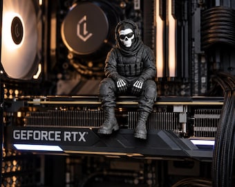 Peut inclure: Une petite figurine de soldat portant un uniforme tactique noir et un masque de crâne blanc, assise sur une carte graphique GeForce RTX noire à l'intérieur d'un boîtier d'ordinateur avec des ventilateurs éclairés.