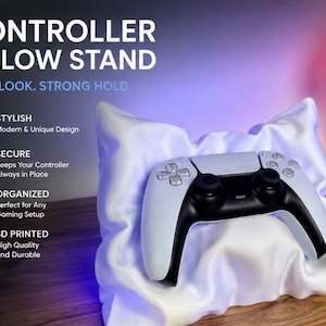 May include: A white, soft-textured controller pillow stand supporting a black and white gaming controller. The text reads: CONTROLLER PILLOW STAND, SOFT LOOK. STRONG HOLD, STYLISH, SECURE, ORGANIZED, and 3D PRINTED with descriptive bullet points.