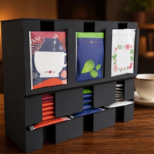Peut inclure: Un organisateur de sachets de thé noir avec plusieurs fentes verticales. La rangée supérieure présente trois sachets de thé distincts aux motifs graphiques colorés, tandis que la rangée inférieure contient des piles de sachets rouges, bleus et blancs.