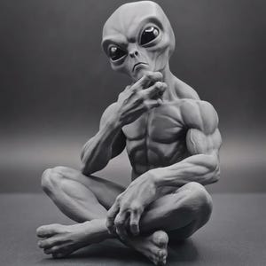 May include: A gray monochromatic sculpture of an extraterrestrial being with a muscular physique, seated in a cross-legged position. The figure has a large head with smooth skin, prominent dark eyes, and one hand resting near its chin.