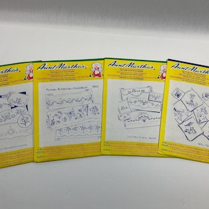 May include: Four Aunt Martha's hot iron transfer packets with yellow borders and white centers. Each packet features blue line art illustrations of embroidery patterns, including floral motifs, butterflies, His and Hers text, and Mexican-themed designs.