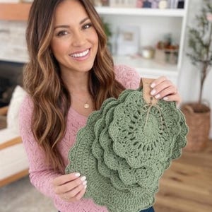 Peut inclure: Un ensemble de napperons au crochet circulaires vert sauge avec un bord festonné. Les napperons sont empilés et fixés avec une étiquette en papier brun attachée par une fine ficelle de jute, mettant en valeur une texture de fil détaillée.