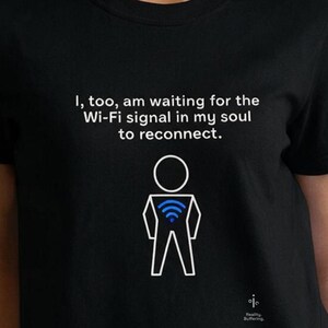 Peut inclure: Un t-shirt noir à manches courtes avec un dessin au trait blanc représentant un personnage bâton portant un symbole Wi-Fi bleu sur la poitrine. Au-dessus, le texte indique : I, too, am waiting for the Wi-Fi signal in my soul to reconnect.
