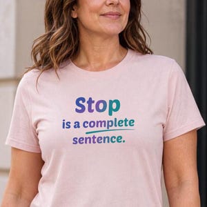 May include: A light pink short-sleeved t-shirt featuring the text "Stop is a complete sentence." printed in a gradient of purple, blue, and teal. The shirt has a crew neckline and a standard fit, showcasing the bold, multi-coloured lettering clearly.