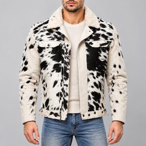 May include: A jacket featuring a black and white cow print pattern with a textured finish. The garment includes a cream-colored faux fur collar, two chest pockets with button closures, and a buttoned hemline. It is worn over a plain cream shirt.