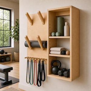 May include: A light-coloured wooden wall-mounted storage unit featuring angled pegs for yoga mats, a row of hooks for resistance bands, and three open shelves holding a foam roller, a water bottle, two towels, a kettlebell, and two dumbbells.