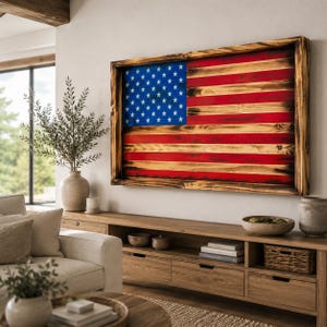 May include: A rectangular wall art piece featuring a wooden American flag with a burnt, rustic finish. The flag displays a blue canton with white stars and horizontal red and natural wood stripes, all enclosed within a thick, dark stained wooden frame.