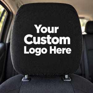 May include: A black car headrest cover featuring the white text Your Custom Logo Here printed in the center. The cover is made of a soft fabric and is designed to fit securely over the headrest of a vehicle seat for a clean appearance.