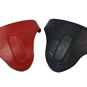 May include: Two curved, molded protective guards, one in deep red and one in black. Each piece features a smooth, solid surface with a central, elongated oval indentation. The items have a wide, contoured top edge and a tapered, rounded bottom section.