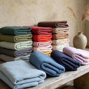 May include: A collection of folded fabric blankets in a variety of colours including dark green, olive, light grey, charcoal, red, orange, pink, yellow, brown, beige, cream, white, light blue, medium blue, navy blue, and soft lavender.