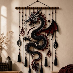 Peut inclure: Une tenture murale représentant un grand dragon en crochet complexe, aux tons noir, crème et rouge foncé. Le dragon est suspendu à une tige en bois horizontale par plusieurs cordons noirs ornés de petites perles rouges, de flammes et de pompons.