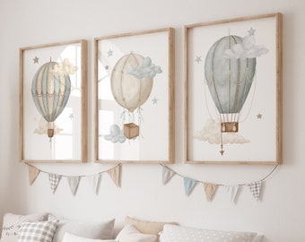 Puede incluir: Tres impresiones enmarcadas de acuarela de globos aerostáticos con nubes y estrellas. Las impresiones están colgadas en una pared blanca sobre un banco de madera con contenedores de almacenamiento. El banco está decorado con almohadas y una jirafa de peluche.