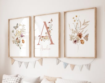 May include: Three framed prints with a floral and butterfly design. The center print features the letter "A" with the name "Amelia" below it. The prints are hung on a white wall above a wooden bench with pillows.