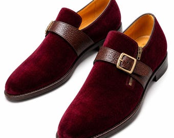 May include: A pair of deep burgundy velvet loafers featuring a dark brown pebbled leather strap across the vamp. Each shoe includes a gold-toned metal buckle, a side zipper detail, a dark brown sole, and a smooth yellow interior lining.