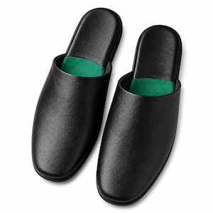 Puede incluir: Un par de zapatillas negras sin cordones con un exterior liso y texturizado y una plantilla de color verde vibrante. Las zapatillas tienen un diseño de punta redondeada y una construcción sencilla abierta por detrás, ofreciendo un aspecto limpio.