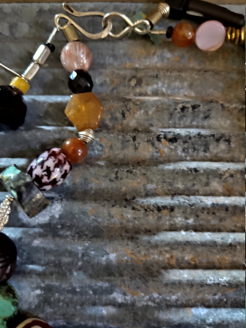 May include: A multi-colored beaded necklace with a silver clasp. The beads are made of various materials, including glass, stone, and metal. The necklace is strung on a brown cord.