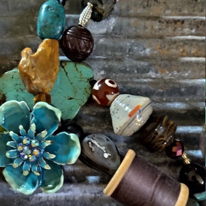 May include: A turquoise blue flower charm with rhinestones, a brown spool of thread, and a variety of colorful beads, including turquoise, brown, orange, and white, strung on a necklace.