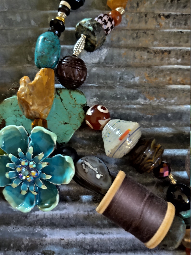 May include: A turquoise blue flower charm with rhinestones, a brown spool of thread, and a variety of colorful beads, including turquoise, brown, orange, and white, strung on a necklace.