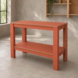 Pode incluir: Uma mesa consola retangular com um acabamento vibrante em laranja terracota e bordas de contraplacado claro expostas. A peça apresenta quatro pernas verticais robustas, uma superfície superior plana e uma prateleira inferior única.