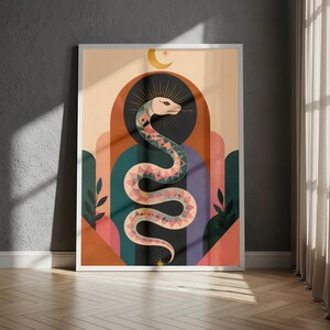 May include: A framed wall art print featuring a central snake with a geometric pattern in shades of pink, orange, and teal. The snake is positioned within a series of layered arches in muted tones, topped by a crescent moon and a small star.