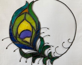 May include: A stained glass peacock feather design with a black metal frame. The feather is a vibrant blue, green, and yellow with a purple eye.